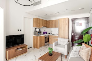 A modern living room with a flat-screen TV, wooden cabinets, a kitchen with a stove and microwave, and a white sofa. - Silkhaus 1bdr Stay Al Maryah Island Near Adgm (Abu Dhabi)
