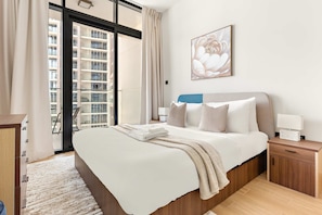A modern bedroom with a large bed, a nightstand, a wooden dresser, and a window with a view of a building. - Silkhaus 1bdr Stay Al Maryah Island Near Adgm (Abu Dhabi)