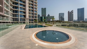 Un edificio moderno con zona de piscina en la azotea, que incluye un jacuzzi circular y una piscina rectangular.