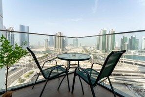 A balcony with a glass table and chairs, overlooking a cityscape with modern buildings and a river. - Silkhaus Elite 1bdr Stay in Al Maryah Island (Abu Dhabi)