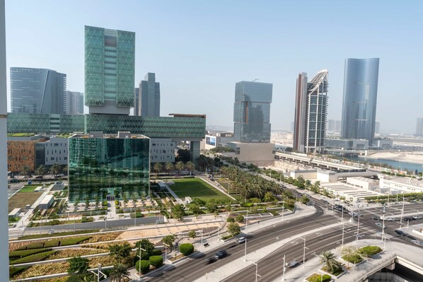 A modern urban landscape with high-rise buildings, a well-maintained plaza with greenery, and a busy road with vehicles. - Silkhaus Elite 1bdr Stay in Al Maryah Island (Abu Dhabi)