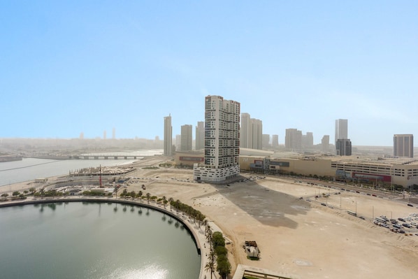 A modern high-rise building with a unique architectural design, situated near a waterfront and a sandy area with a parking lot. - Silkhaus Bayside 1bdr Stay Marina Bay Tower (Abu Dhabi)