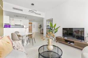 A modern living room with a glass coffee table, a sofa, a TV, and a dining area with chairs and a table. - Silkhaus Bayside 1bdr Stay Marina Bay Tower (Abu Dhabi)