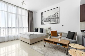 Ein modernes Schlafzimmer mit Bett, Sofa, Couchtisch und einem großen Fenster mit transparenten Vorhängen.