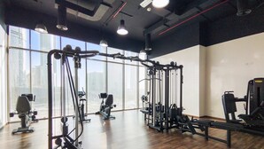 A gym with exercise equipment, large windows, and a wooden floor. - Silkhaus 1bdr in Horizon Tower Al Fay Park Near (Abu Dhabi)