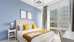 A modern hotel room with a large bed, a bedside table, a desk, and a view of the city through large windows. - Silkhaus 1bdr in Horizon Tower Al Fay Park Near (Abu Dhabi)