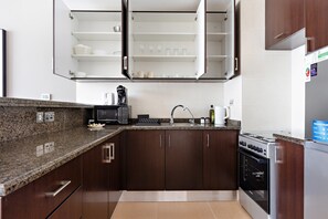 A kitchen with dark wooden cabinets, a granite countertop, a stainless steel oven, and a microwave. - Silkhaus in Yasmine Near Golf Course Club (Abu Dhabi)