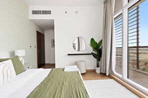 A hotel room with a bed, a bedside table, a lamp, a mirror, a potted plant, and a large window with a view of the city. - Silkhaus in Yasmine Near Golf Course Club (Abu Dhabi)