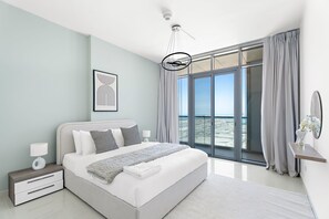 Ein modernes Schlafzimmer mit einem großen Bett, einem Nachttisch, einer Wandleuchte und einem Deckenventilator. Ein großes Fenster mit Vorhängen.