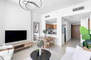 Ein modernes Wohnzimmer mit einem Flachbildfernseher, einem runden Couchtisch mit einer Vase und Pflanzen, einem weißen Sofa und einem Essbereich mit einem Holztisch und Stühlen.
