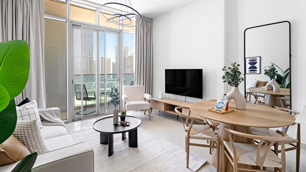 Ett modernt vardagsrum med en soffa, ett soffbord, ett matbord och stolar. En platt-TV är monterad på väggen och det finns ett stort fönster med gardiner.