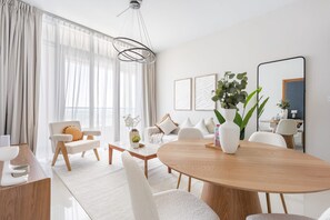 A modern living room with a round wooden dining table, white sofas, and a large window with sheer curtains. - Silkhaus 2bdr Retreat Julphar Tower Al Reem (Abu Dhabi)