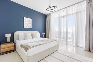 A modern bedroom with a large bed, a nightstand, a wall art piece, and a view of the outdoors through sheer curtains. - Silkhaus 2bdr Retreat Julphar Tower Al Reem (Abu Dhabi)