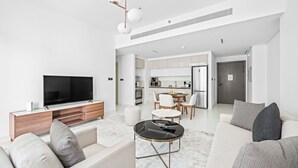 A modern living room with a flat-screen TV, a wooden entertainment unit, a round coffee table, and a sofa with patterned cushions. - Silkhaus Sea View 1bdr Marina Vista Tower (Dubai)