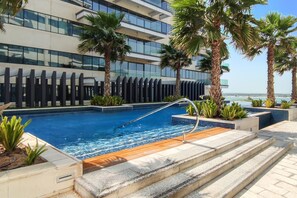 Um hotel moderno com piscina, palmeiras e vista para o mar.