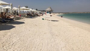 A beach with sun loungers and umbrellas, a lifeguard stand, and a clear view of the sea. - Silkhaus Mayan Lux 1BR Yas Island Beach Access (Abu Dhabi)
