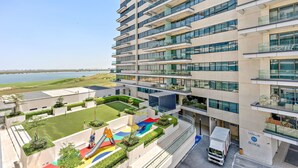 A modern multi-story building with balconies, a parking area, and a view of a body of water. - Silkhaus Mayan Lux 1BR Yas Island Beach Access (Abu Dhabi)