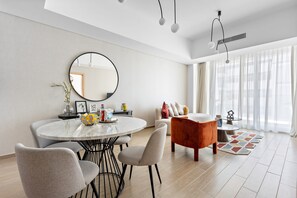 Ein modernes Wohnzimmer mit einem runden Esstisch, grauen Stühlen, einem roten Sessel und einem großen Fenster mit durchsichtigen Vorhängen.