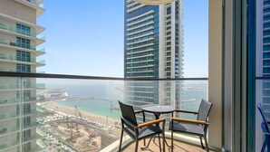 A balcony with a glass railing, a round table with two chairs, and a view of a beach and high-rise buildings. - Silkhaus 1bdr w Beach Access Marina Vista (Dubai)