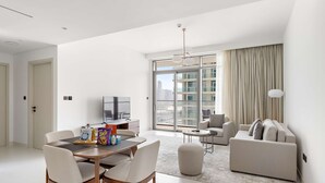 A modern living room with a dining area, a sofa, and a TV. - Silkhaus 1bdr w Beach Access Marina Vista (Dubai)