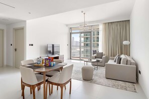 A modern living room with a dining area, a sofa, and a TV. - Silkhaus 1bdr w Beach Access Marina Vista (Dubai)