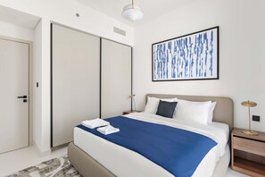 A modern hotel room with a large bed, a wardrobe, a bedside table with a lamp, and a wall art piece. - Silkhaus 1bdr w Beach Access Marina Vista (Dubai)