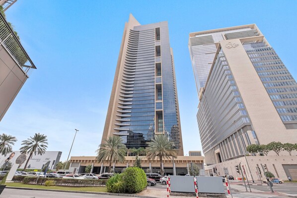 A modern high-rise building with a sleek, reflective facade and a prominent logo on the side. - Silkhaus Sky Gardens Homestyle Studio Difc (Dubai)