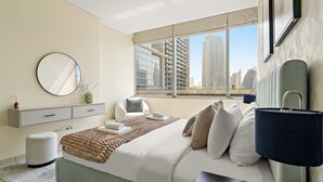 Een moderne hotelkamer met een groot bed, een nachtkastje, een lamp, een ronde spiegel, een raam met uitzicht op de stad en een klein zithoekje.