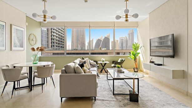 Een moderne woonkamer met een bank, salontafel en stoelen, grote ramen met uitzicht op de stad, en een flatscreen televisie aan de muur.
