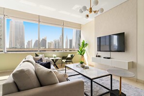 Ein modernes Wohnzimmer mit Sofa, Couchtisch und Fernseher, großen Fenstern mit Blick auf die Stadt und einer Heizung.