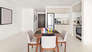 A modern kitchen with white cabinets, a stainless steel refrigerator, and a dining area with a wooden table and two chairs. - Silkhaus Cozy 1bdr in Marina Vista Private Beach (Dubai)