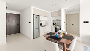 A modern kitchen with white cabinets, a stainless steel refrigerator, and a dining area with a wooden table and chairs. - Silkhaus Cozy 1bdr in Marina Vista Private Beach (Dubai)