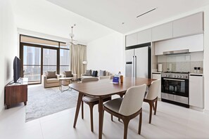 A modern living room with a dining area, kitchen, and large windows. - Silkhaus Large 2BR Private Beach Marina Vista (Dubai)