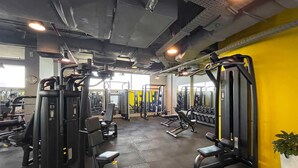A gym with various exercise machines, a clock on the wall, and a yellow wall. - Silkhaus Luxury Studio Sky Gardens Difc Views (Dubai)