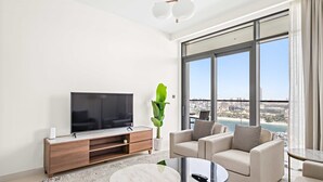 Ein modernes Wohnzimmer mit großem Fernseher, bequemen Sitzmöglichkeiten, einem Couchtisch und einem großen Fenster mit Blick auf die Stadt.