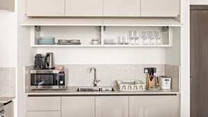Eine moderne Küche mit weißen Schränken, einer Mikrowelle, einem Toaster, einem Spülbecken und Regalen mit Geschirr und Gläsern.
