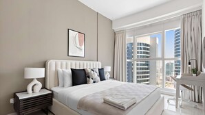 Ett modernt hotellrum med en stor säng, ett nattduksbord med en lampa, utsikt över staden genom stora fönster och ett piano i hörnet.