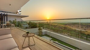 A modern balcony with a glass railing overlooking a grassy landscape and a sunset. - Silkhaus Beach Villa Private Pool 3BR Maid (Abu Dhabi)