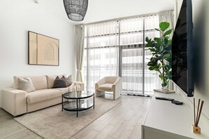 Ein modernes Wohnzimmer mit Sofa, Sessel, Couchtisch und einem großen Fenster mit transparenten Vorhängen.