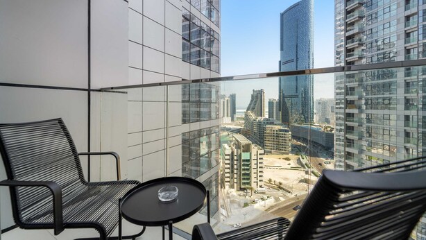 A balcony with a glass railing, two black chairs, and a small table. - Silkhaus 1bdr in Reem Island in New Modern Tower (Abu Dhabi)