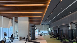 A modern gym with various exercise equipment, large windows, and a striped floor. - Silkhaus 1bdr in Reem Island in New Modern Tower (Abu Dhabi)