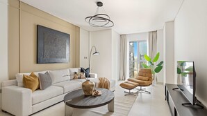 A modern living room with a white sofa, a round coffee table, a brown armchair, a TV on a stand, and a large window with a view of buildings. - Silkhaus 1bdr in Reem Island in New Modern Tower (Abu Dhabi)