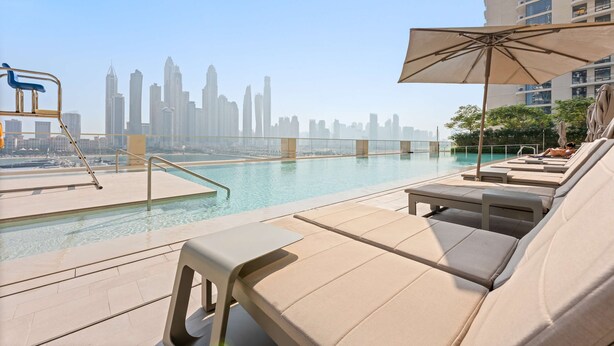 Piscina en la azotea con sillas de descanso y una sombrilla, con vista al horizonte de una ciudad.
