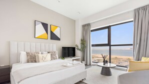 A modern hotel room with a large bed, a flat-screen TV, a small table, and a view of the beach. - Silkhaus Sea View Studio in Pixel Private Beach (Abu Dhabi)