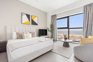 A modern hotel room with a large bed, a flat-screen TV, a small table, and a view of the beach. - Silkhaus Sea View Studio in Pixel Private Beach (Abu Dhabi)