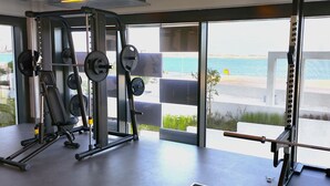 A gym with weightlifting equipment and large windows overlooking a beach. - Silkhaus Sea View Studio in Pixel Private Beach (Abu Dhabi)