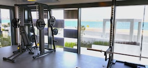 A gym with weightlifting equipment and large windows overlooking a beach. - Silkhaus Sea View Studio in Pixel Private Beach (Abu Dhabi)