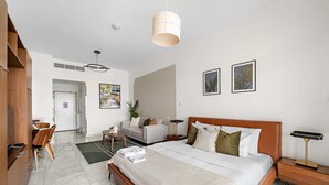 A modern hotel room with a large bed, a desk, and a sofa. There are two framed pictures on the wall and a plant on the desk. - Silkhaus Chic Studio in Palm Jumeirah Sea View (Dubai)