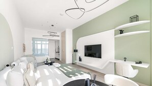 A modern living room with a sofa, a dining table with candles, and a TV mounted on the wall. - Silkhaus Chic Studio With Pool and Gym (Dubai)