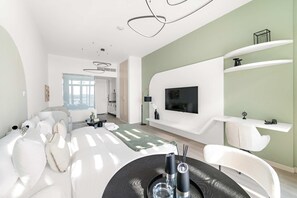 A modern living room with a sofa, a dining table with candles, and a TV mounted on the wall. - Silkhaus Chic Studio With Pool and Gym (Dubai)